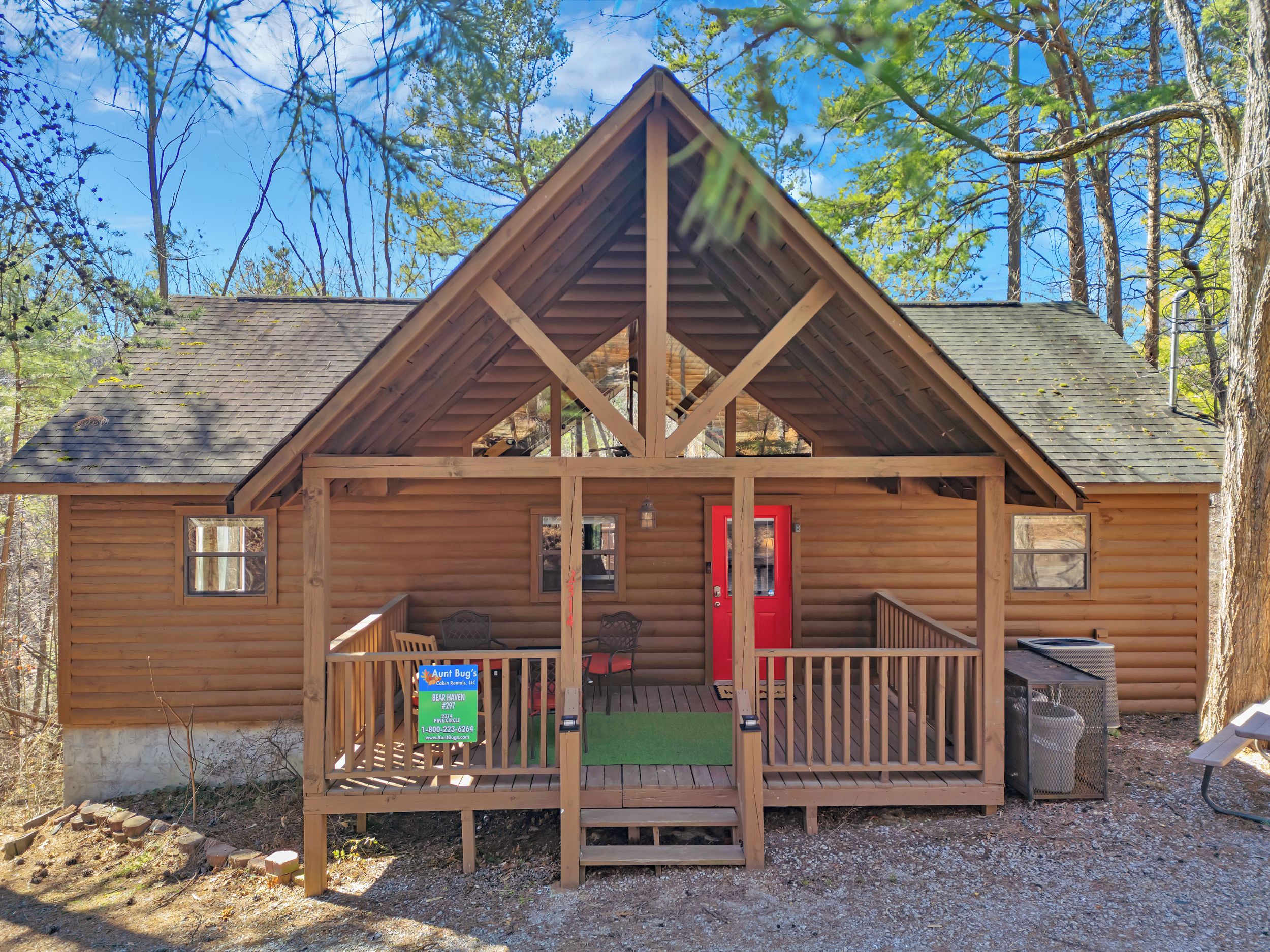 A wooden cabin with a porch, a red door, and a sign for Aunt Bug's Bear Haven.