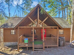 A wooden cabin with a porch, a red door, and a sign for Aunt Bug's Bear Haven.