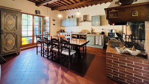 A rustic kitchen with wooden beams, a dining area with a table and chairs, and a brick fireplace.