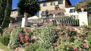 A stone building with a balcony, surrounded by lush greenery and flowering plants.