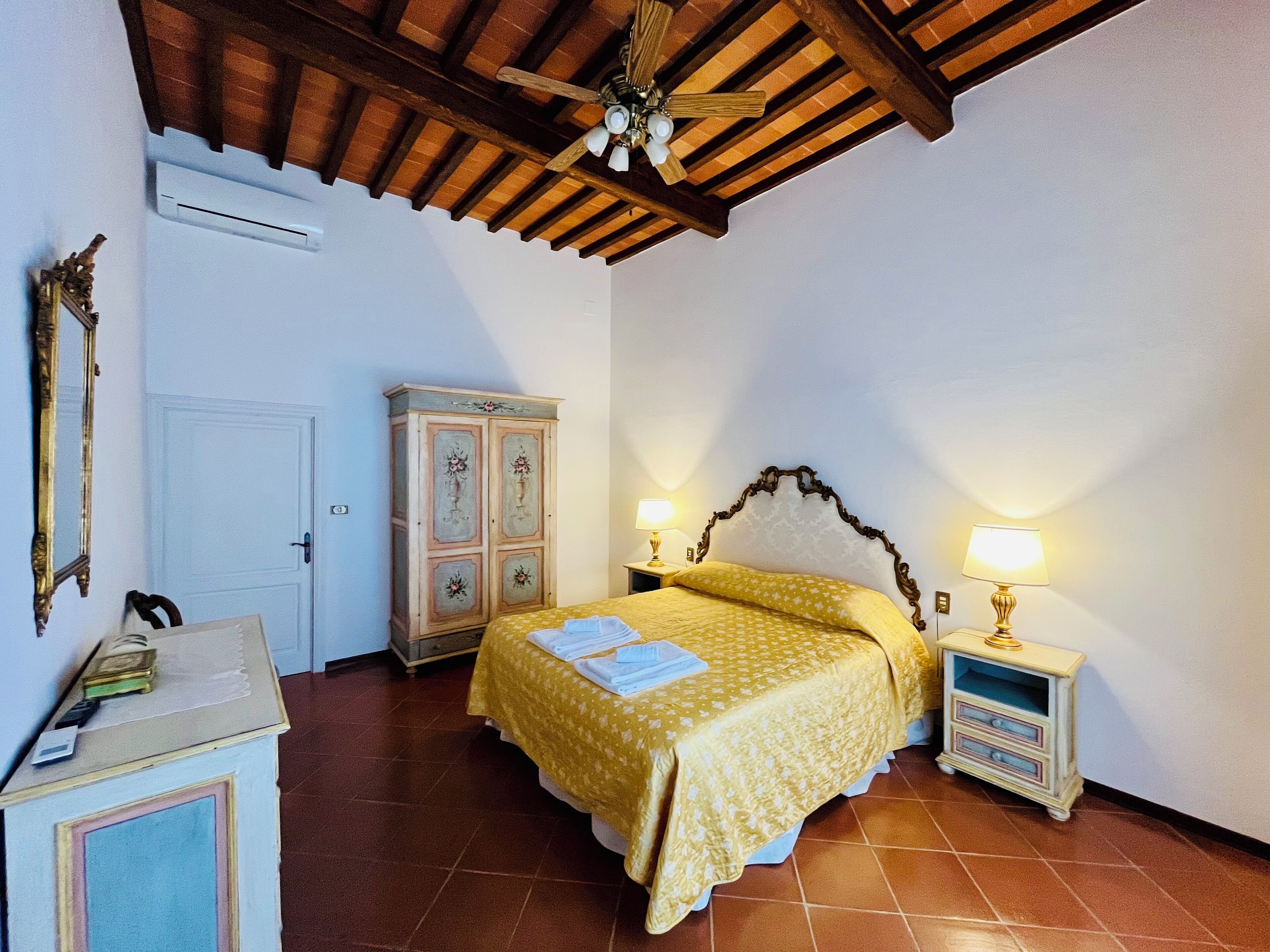 A bedroom with a bed, two bedside tables with lamps, a wardrobe, a ceiling fan, and a door.