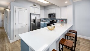 A modern kitchen with white cabinets, stainless steel appliances, and a central island with stools. - Ocean Front 3 BR/3BA/Ground Floor walk out Updated (Fort Walton Beach)