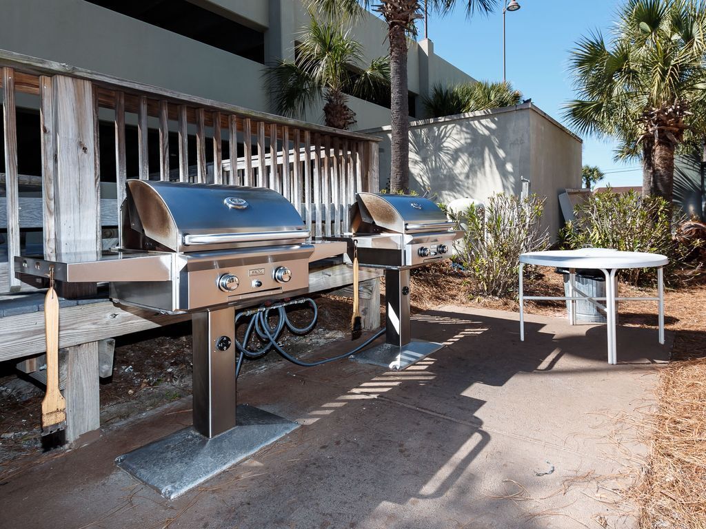 An outdoor barbecue area with two grills, a table, and a trash bin.