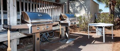 An outdoor barbecue area with two grills, a table, and a trash bin.