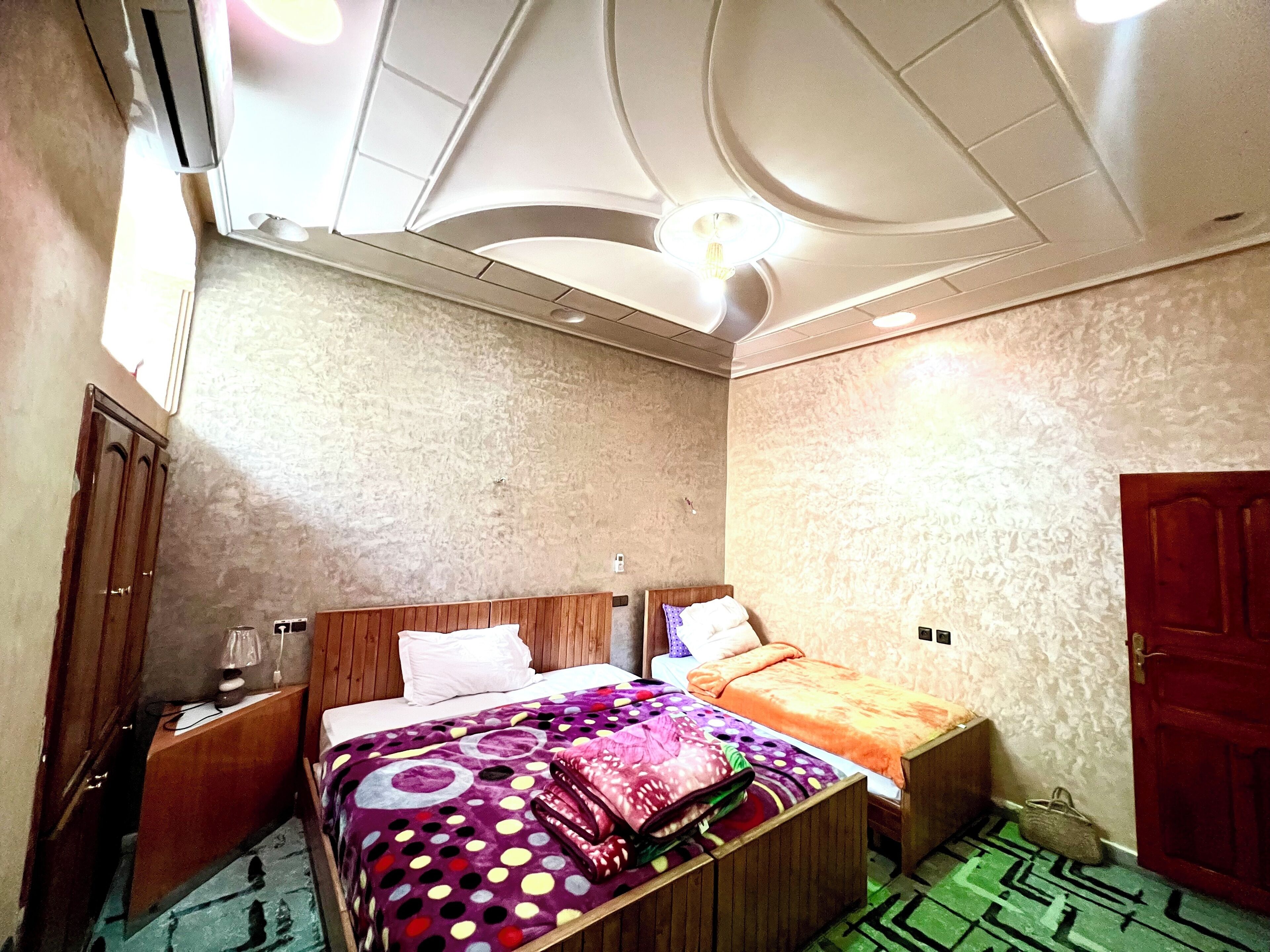A bedroom with two beds, a wooden wardrobe, a desk, and a patterned rug.