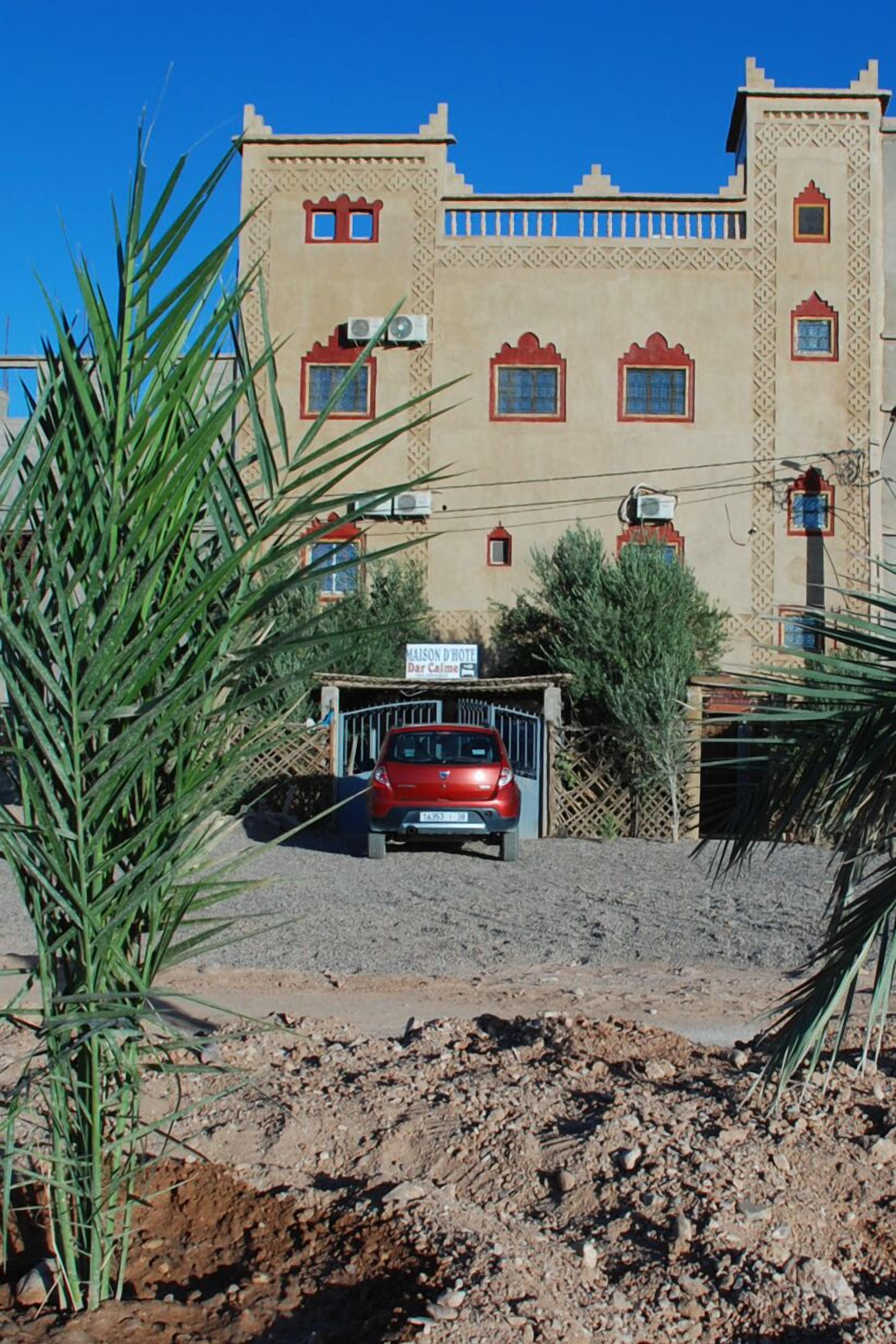 Un edificio con un letrero que dice "MAISON D'OTEL" y un auto rojo estacionado adelante.