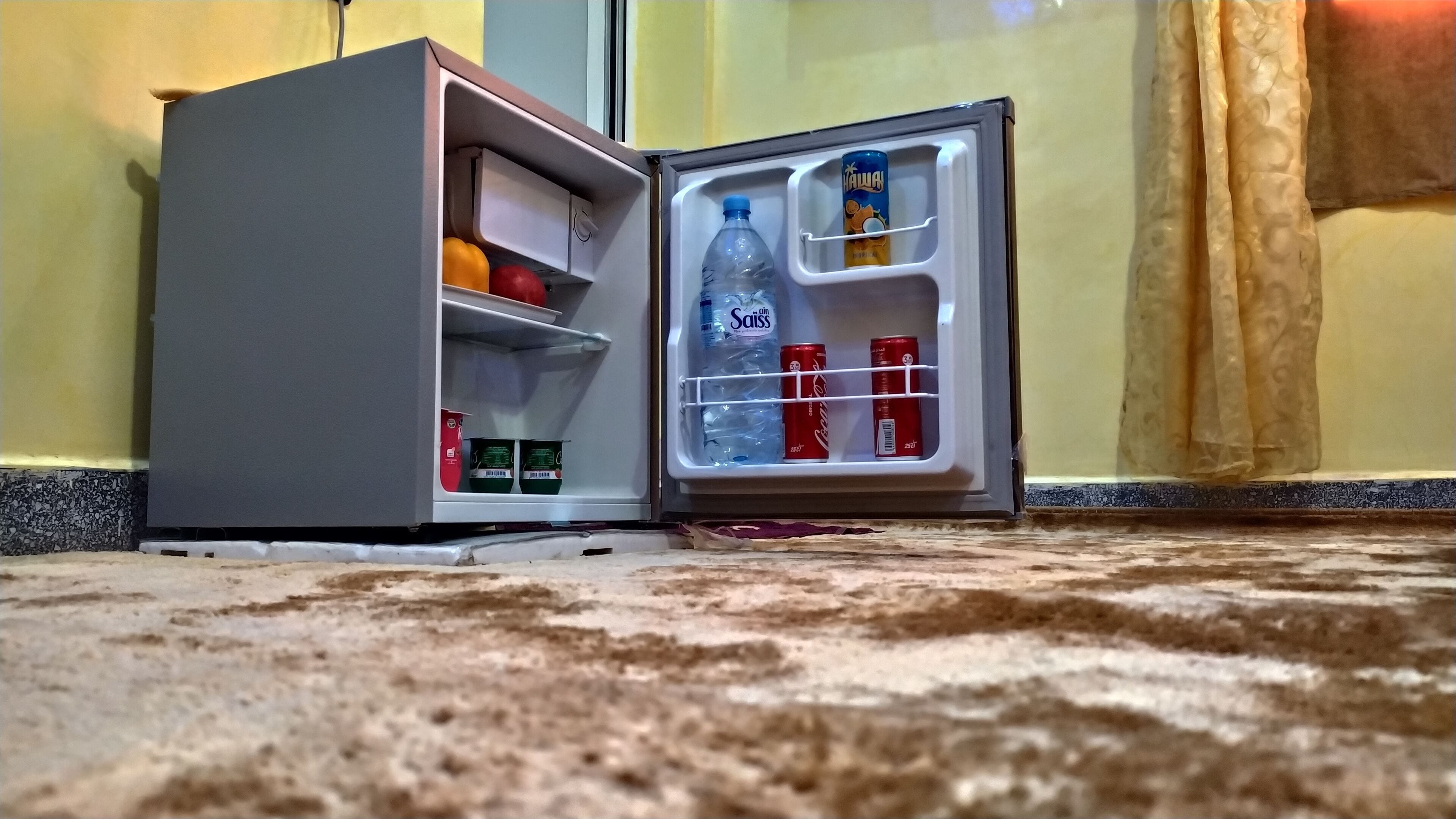 Un petit réfrigérateur contenant une bouteille d’eau, une canette de soda et un carton de lait.