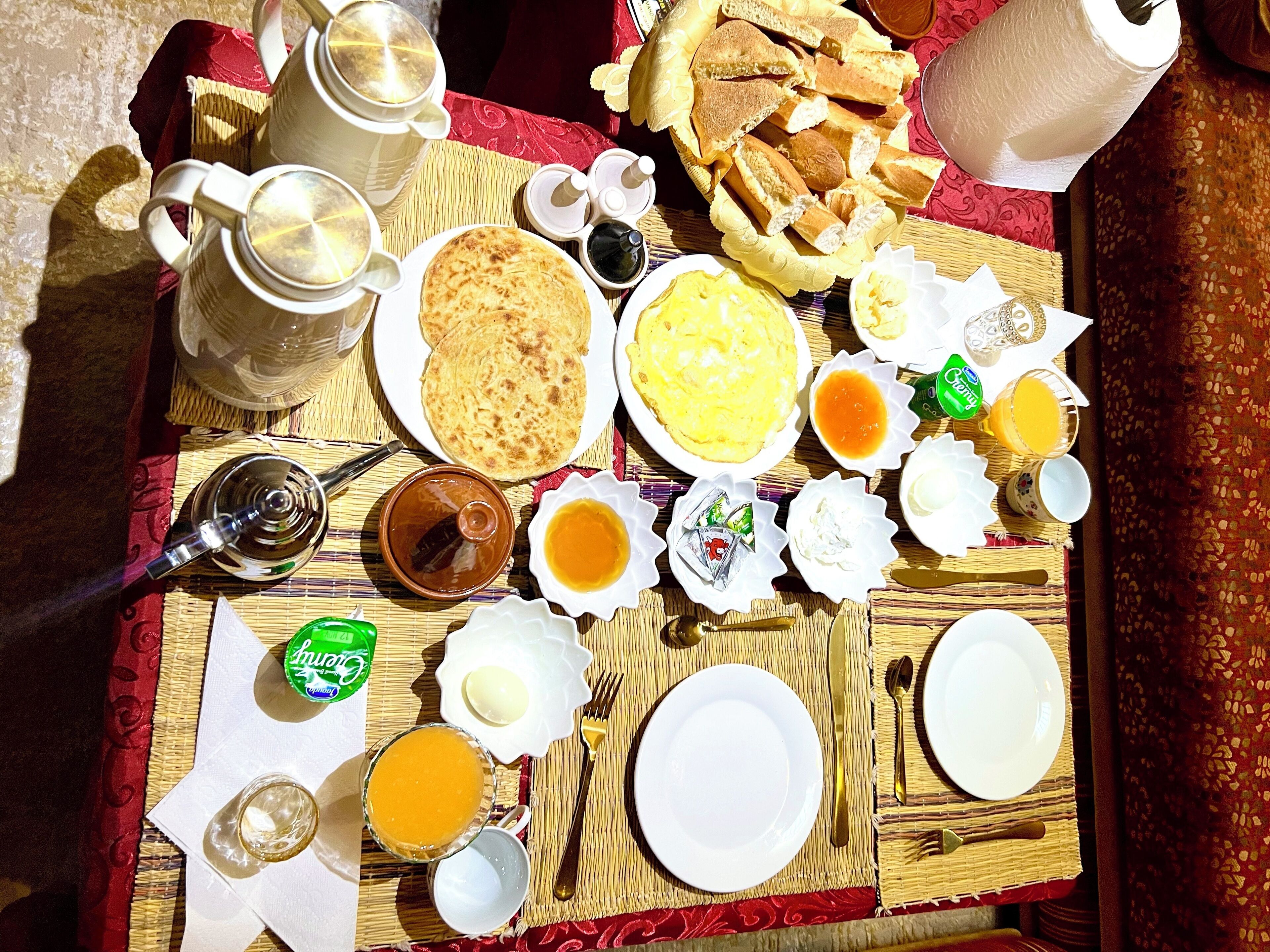 A breakfast spread with various dishes and utensils on a woven mat.