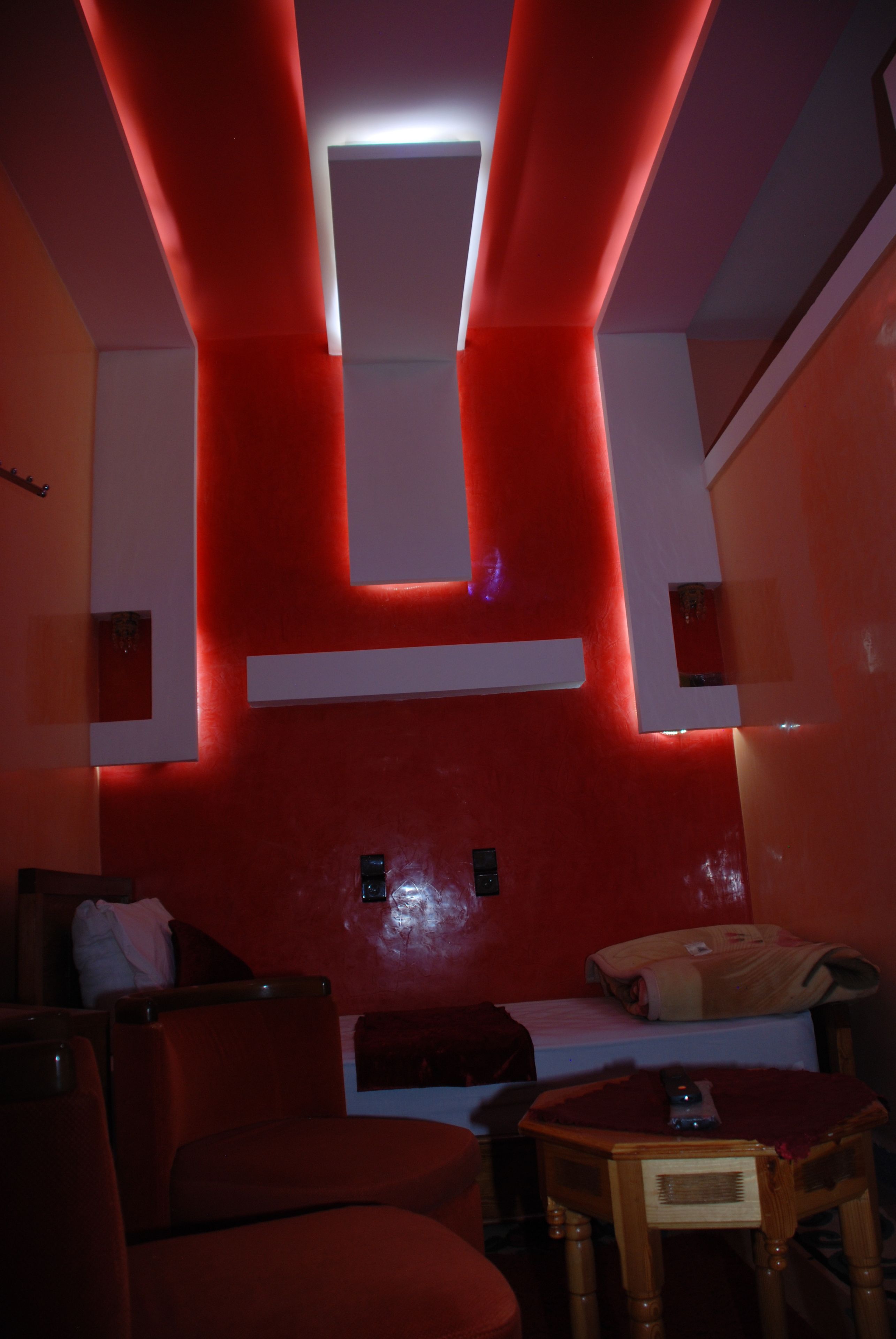 A modern hotel room with red walls, a flat-screen TV, a wooden table, and a sofa.