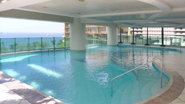 An indoor swimming pool with clear views of the ocean and a balcony area. - Baywatch Tower (Manila)