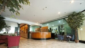 A hotel lobby with a reception desk, seating area, and a large potted plant. - Baywatch Tower (Manila)