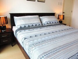 Cama bem arrumada com roupa de cama estampada, duas luminárias de cabeceira e cabeceira escura.