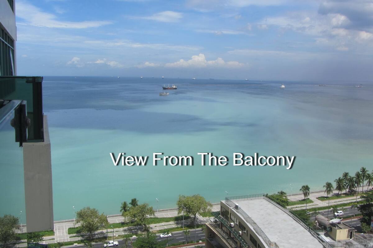 Blick von einem Balkon auf das ruhige Meer mit mehreren Booten, einem klaren Himmel und einer fernen Uferlinie mit Palmen.