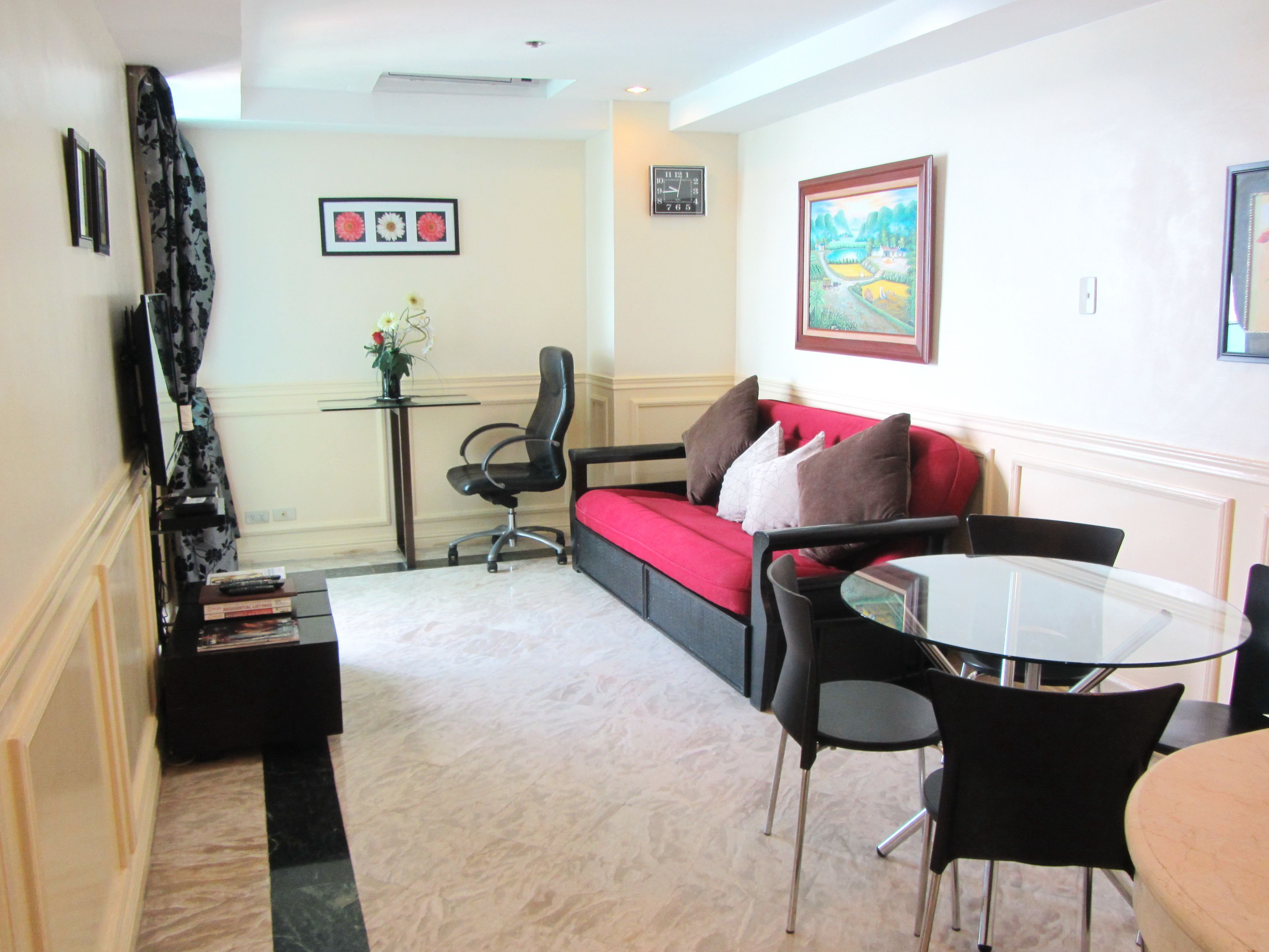 A living room with a red sofa, black chairs, a glass coffee table, a TV, and a painting on the wall.