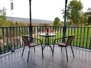 Un balcon avec deux fauteuils en osier et une petite table ronde, donnant sur un paysage verdoyant et vallonné.