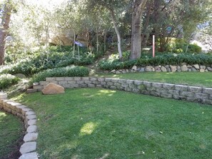 Un jardín ajardinado con un muro de piedra, una zona de césped y varios árboles.