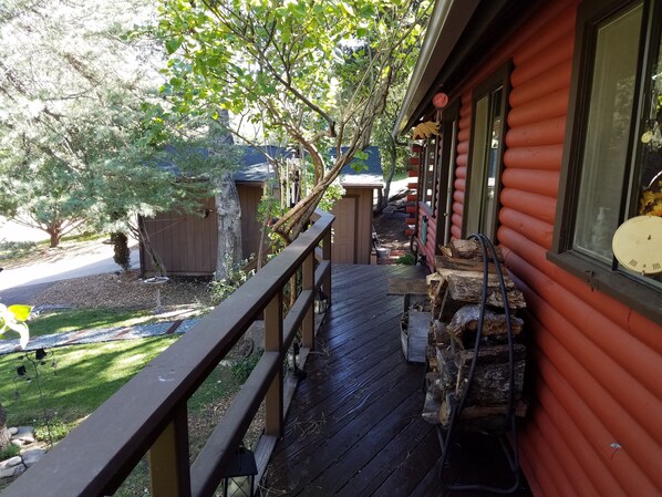A wooden deck with a railing, a stone planter, and a small garden area with a tree and a metal sculpture. - Charming log cabin surrounded by the hills of the Cleveland National Forest (Pine Valley)