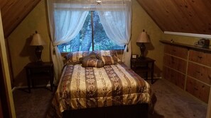 A cozy attic bedroom with a large bed, two bedside tables with lamps, a wooden dresser, and a window with sheer curtains. - Charming log cabin surrounded by the hills of the Cleveland National Forest (Pine Valley)