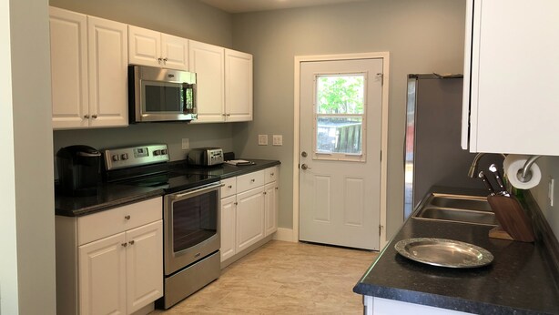 A modern kitchen with white cabinets, stainless steel appliances, and a black countertop. - 1st Class Rentals Munson Manor IV  at Columbia Street (Oneonta)