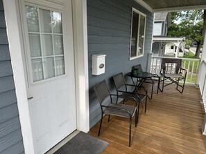 Une véranda avec un plancher en bois, une porte blanche et une petite table entourée de chaises.