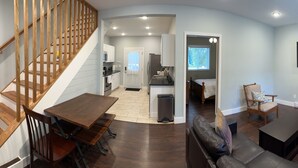 A modern living room with a wooden staircase, a dining area, a kitchen, and a bedroom. - 1st Class Rentals Munson Manor IV  at Columbia Street (Oneonta)