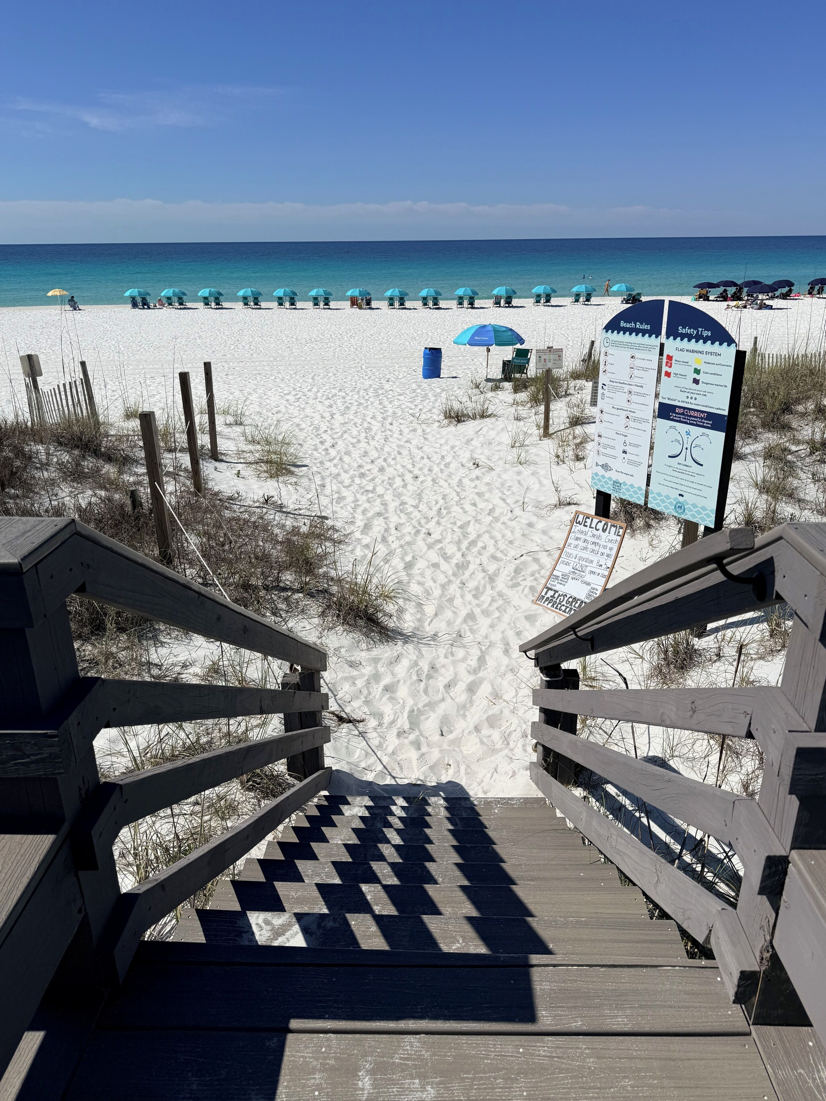 A wooden boardwalk leading to a sandy beach with a clear view of the ocean.