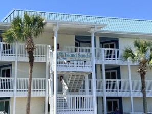 A multi-story hotel with balconies, palm trees, and a sign reading 'Island Sands 862 Scollop Court.'