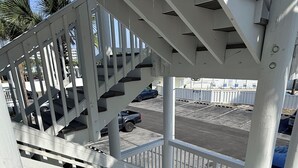 Un escalier blanc mène à un espace de stationnement d’où l’on peut admirer les voitures garées et un ciel dégagé.