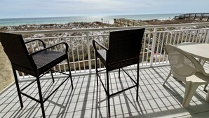 Un balcon avec des fauteuils en osier et une table donnant sur une plage, elle-même bordée d’une promenade en bois.