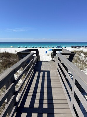 A wooden boardwalk leading to a beach with umbrellas and a clear blue sky.