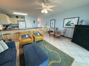 A living room with a sofa, armchairs, a coffee table, a dining table with chairs, a ceiling fan, and a kitchen area in the background. - #204- GULF FRONT, 2ND FLOOR! NOW BOOKING SPRING AND SUMMER! BCH SERVICE INCL.! (Fort Walton Beach)