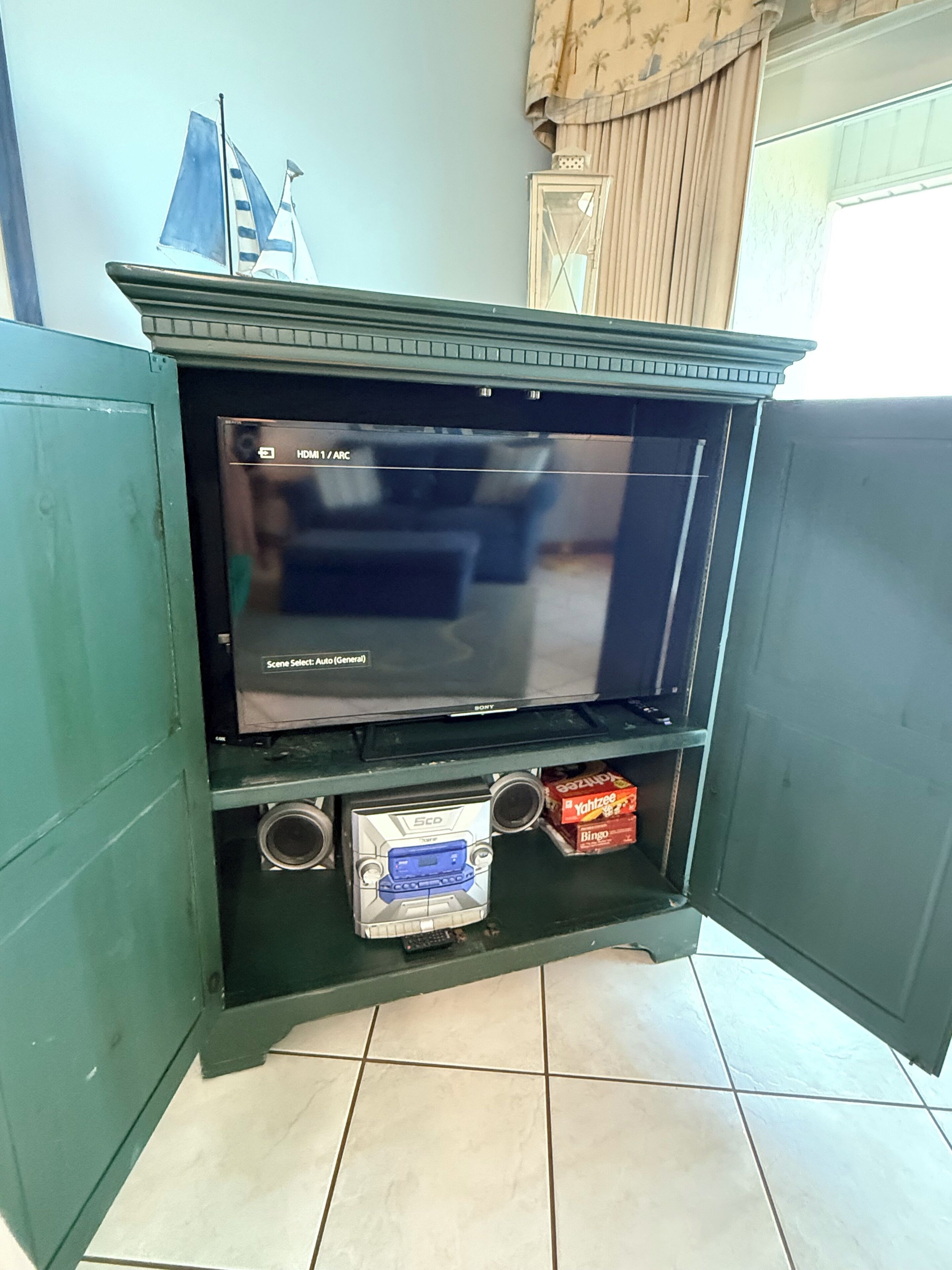 A television with a 'Scene Select: Auto (General)' setting, a small shelf with a cassette player, and a box of Bingo cards.