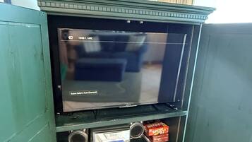 A television with a 'Scene Select: Auto (General)' setting, a small shelf with a cassette player, and a box of Bingo cards.