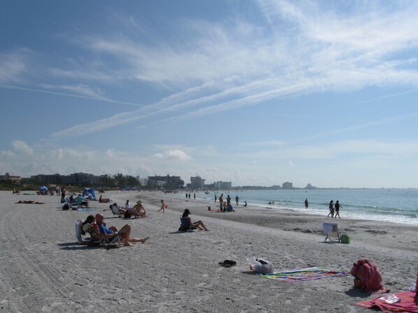 Een strand met mensen die zonnebaden en zwemmen, parasols en ligstoelen.