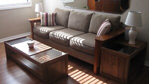 Una sala de estar con un sofá, dos mesitas de noche con lámparas, una mesa de centro y un aparador de madera.