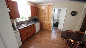 A compact kitchen with wooden cabinets, a microwave, and a sink. There is a dining area with a table and chairs. - Koreana Apartments No.2 (Decorah)