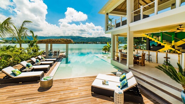 A luxurious resort with an infinity pool, wooden deck, and a dining area with a staircase. - 5 BDR LUX MODERN BEACHFRONT VILLA PRIVATE INFINITY POOL & OCEAN VIEWS STAFF (Montego Bay)