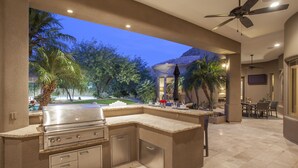 An outdoor kitchen with a built-in grill, surrounded by a patio area with seating and a view of the backyard.