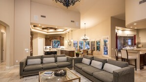 A spacious living room with a large sectional sofa, a glass coffee table, and a kitchen area in the background.
