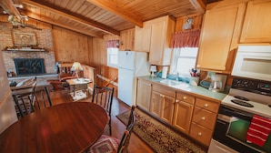 Un intérieur en bois comprenant une table à manger, des chaises, une cheminée, un réfrigérateur et une cuisinière.