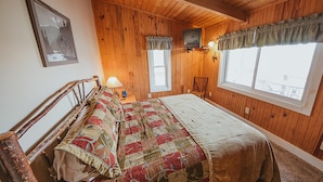 Une chambre aux murs lambrissés, avec un lit, un téléviseur fixé au mur et une fenêtre avec des rideaux.
