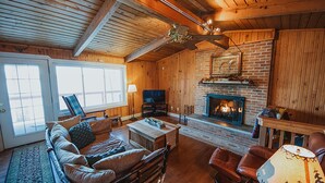 Un salon chaleureux avec une cheminée, des murs en bois et un ventilateur de plafond.