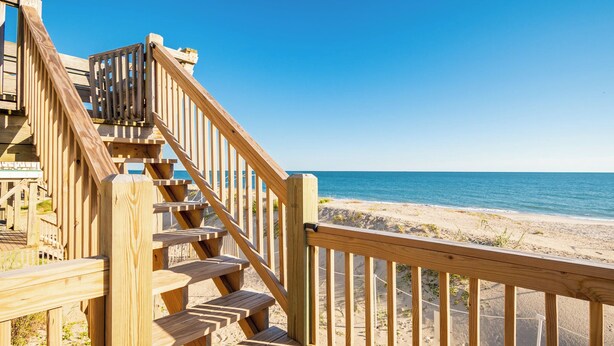 A wooden staircase leading to a beach with clear skies. - A Villa Roja: Oceanfront Home with Incredible Views, Deck, Open Concept (Oak Island)