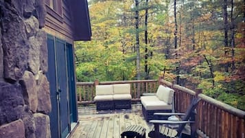Une terrasse en bois avec des murs en pierre, un canapé et deux fauteuils.