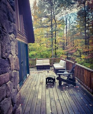 Une terrasse en bois avec des murs en pierre, un canapé et deux fauteuils.