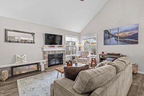 A spacious living room with a fireplace, a large sofa, a television, and a scenic mountain view.