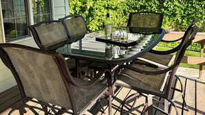 Un área de comedor al aire libre con una mesa de vidrio y sillas de metal, una botella de vino y un vaso de agua sobre la mesa.