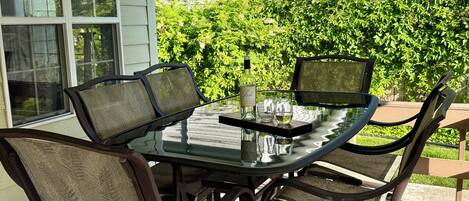 An outdoor dining area with a glass table and metal chairs, a bottle of wine, and a glass of water on the table.