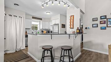 A modern kitchen with a central island, bar stools, and a hanging light fixture.