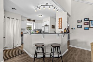 A modern kitchen with a central island, bar stools, and a hanging light fixture.